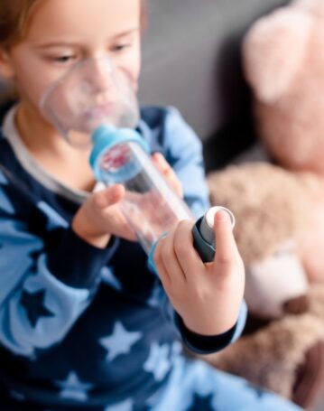 selective focus of sick kid using inhaler with spacer near soft toys